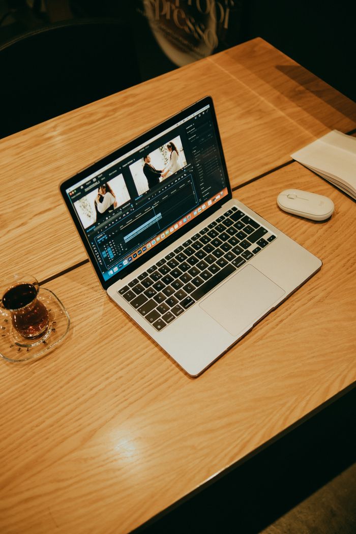 A laptop on a wooden table in a coffee shop, displaying video editing software for creative work.